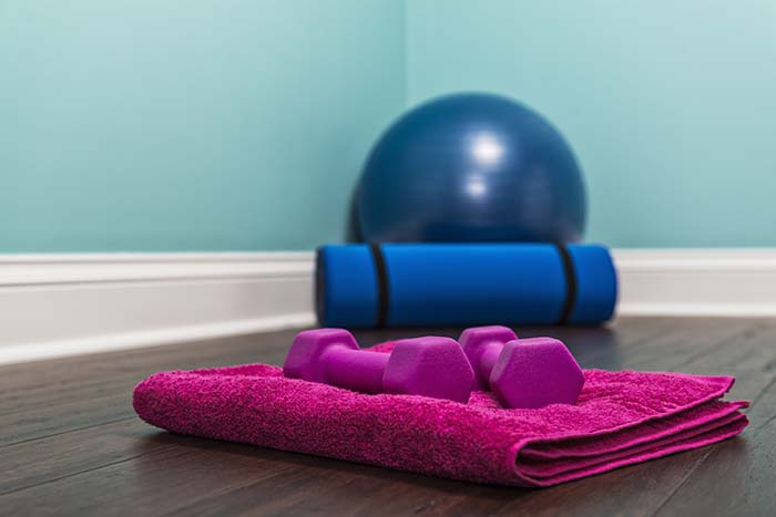 A pair of hand weights on towel with yoga ball and mat at home.