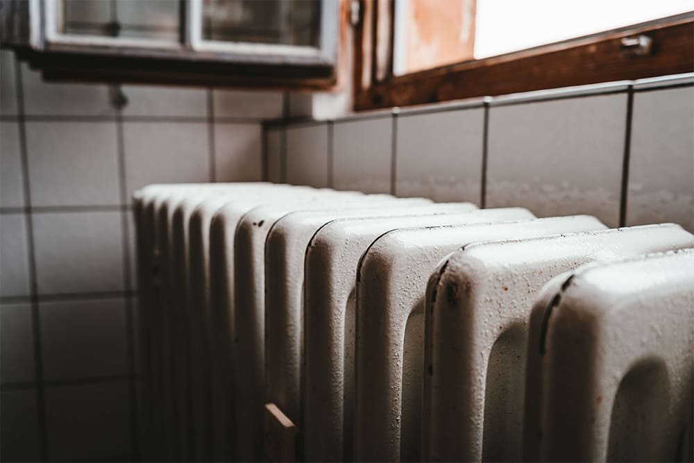 An older white radiator sits in a white-tiled room.