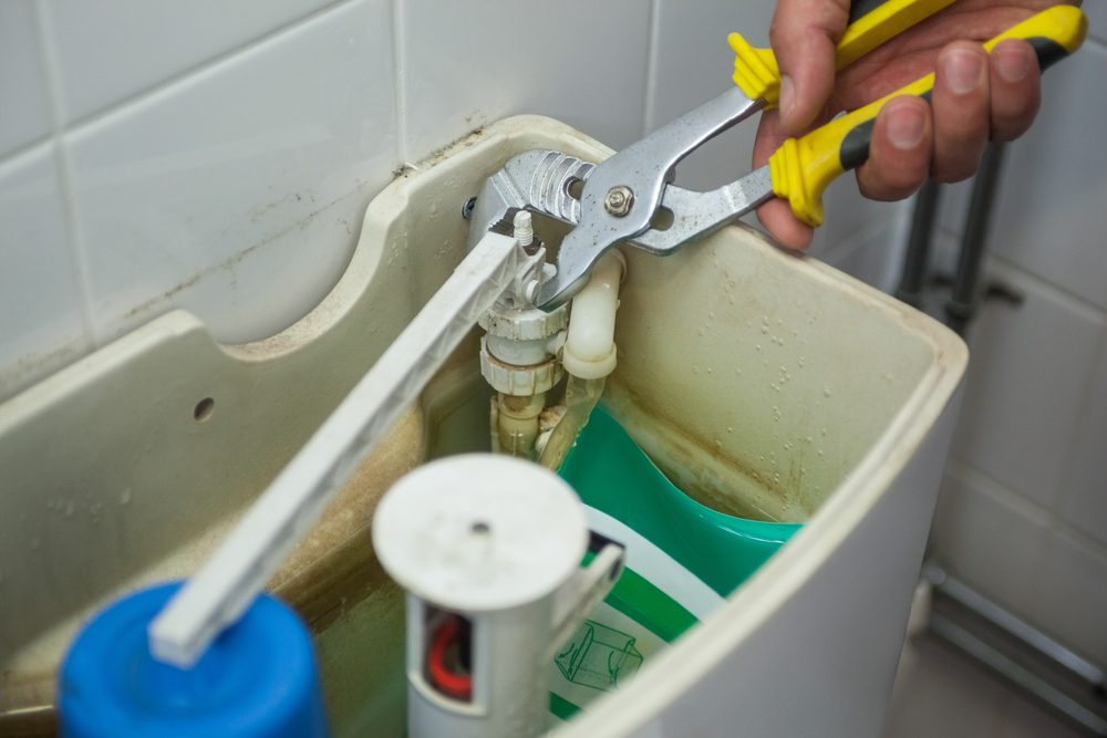 A homeowner using a wrench to fix something in the toilet tank